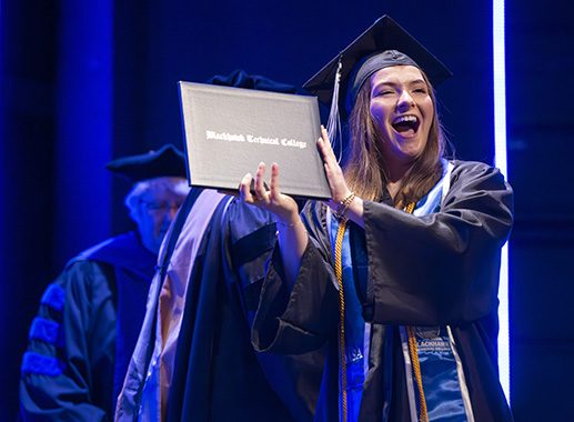 Female graduate holding up diploma at commencement